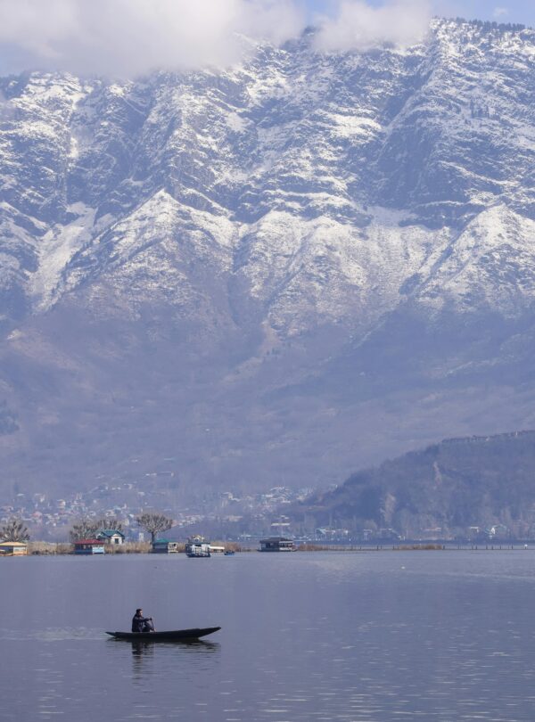Tranquil scene of a boat on Dal Lake with snow-capped Zabarwan mountains in Srinagar.